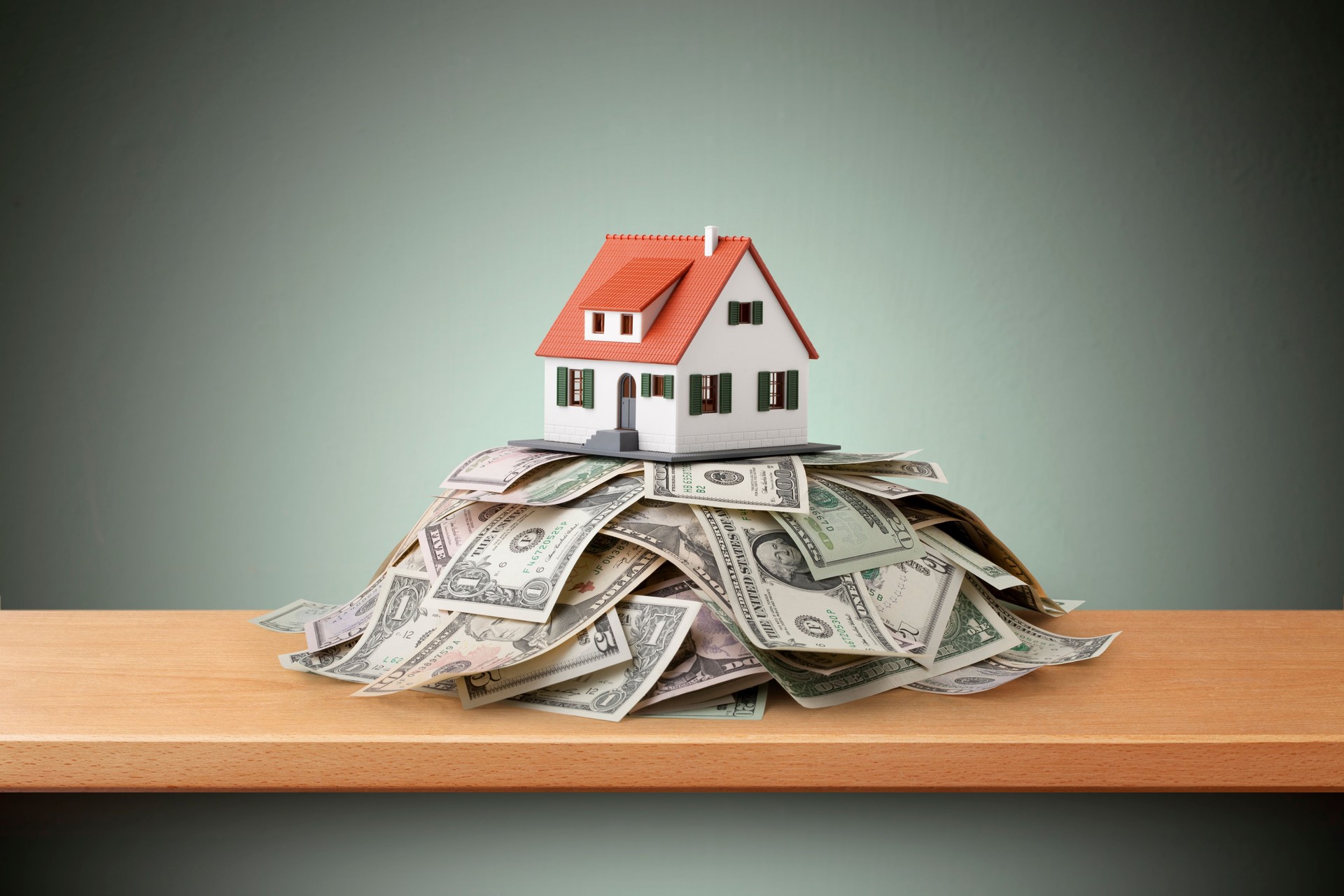 Miniature model house standing on a heap of dollar bills